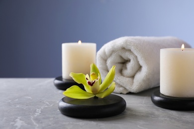 Photo of Spa stones with exotic flower and burning candles on grey table, space for text