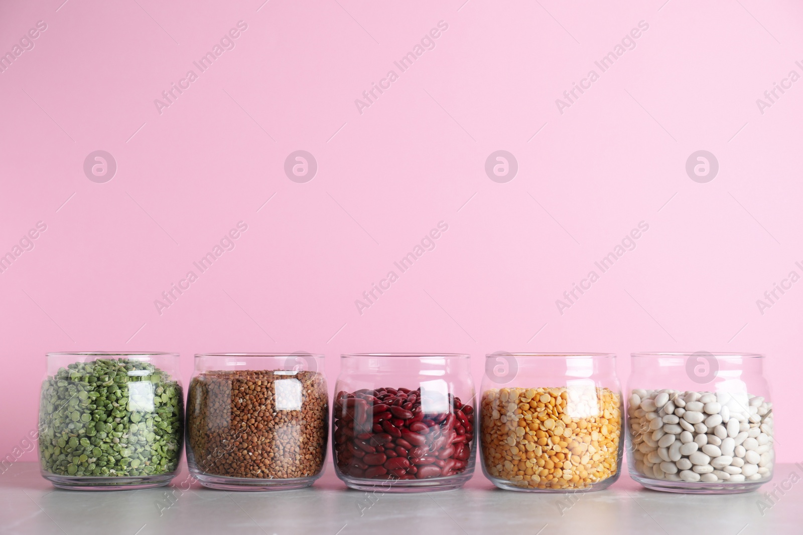 Photo of Glass jars with different types of groats on grey marble table