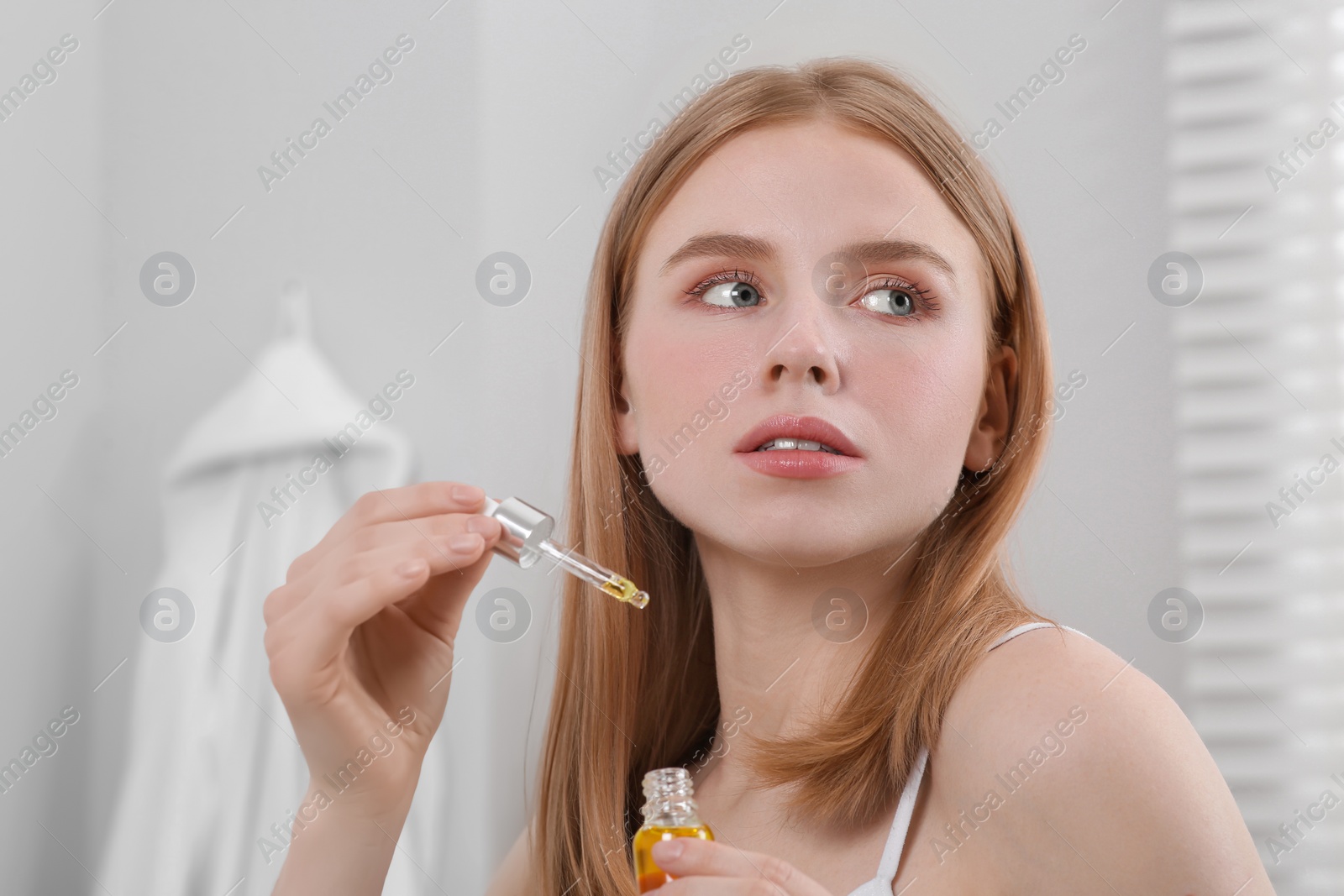 Photo of Young woman with bottle of essential oil in bathroom