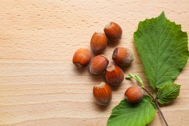 Photo of Tasty hazelnuts and green leaves on wooden table, top view. Space for text
