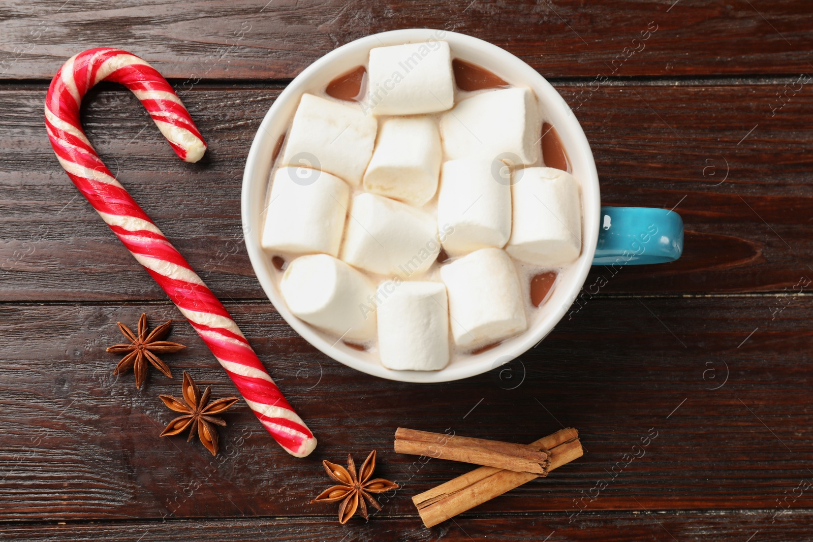 Photo of Tasty hot chocolate with marshmallows, candy cane and spices on wooden table, flat lay