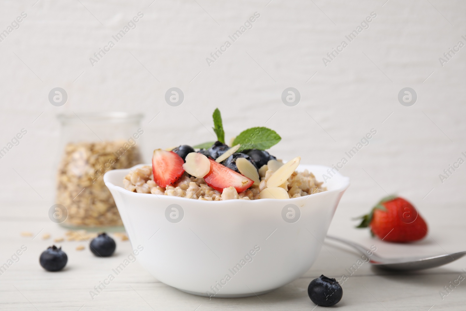 Photo of Tasty oatmeal with strawberries, blueberries and almond petals in bowl on white wooden table