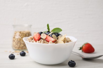 Photo of Tasty oatmeal with strawberries, blueberries and almond petals in bowl on white wooden table