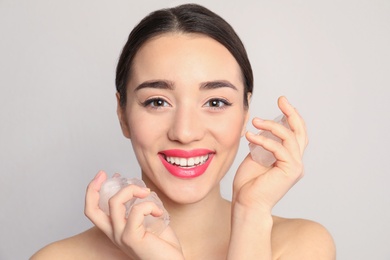 Young woman with ice cubes on light background. Skin care