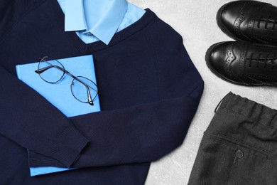 Stylish school uniform for boy, glasses and notebook on grey background, flat lay