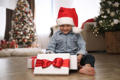 Cute little boy opening gift box in room decorated for Christmas