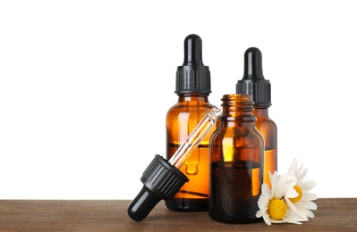 Photo of Bottles of herbal essential oils, pipette and chamomile flowers on wooden table, white background