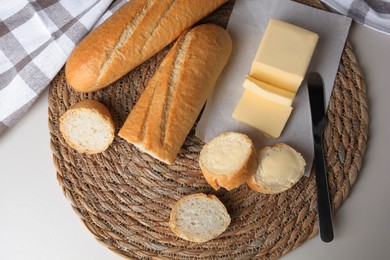 Photo of Tasty cut baguette with fresh butter on white table, flat lay