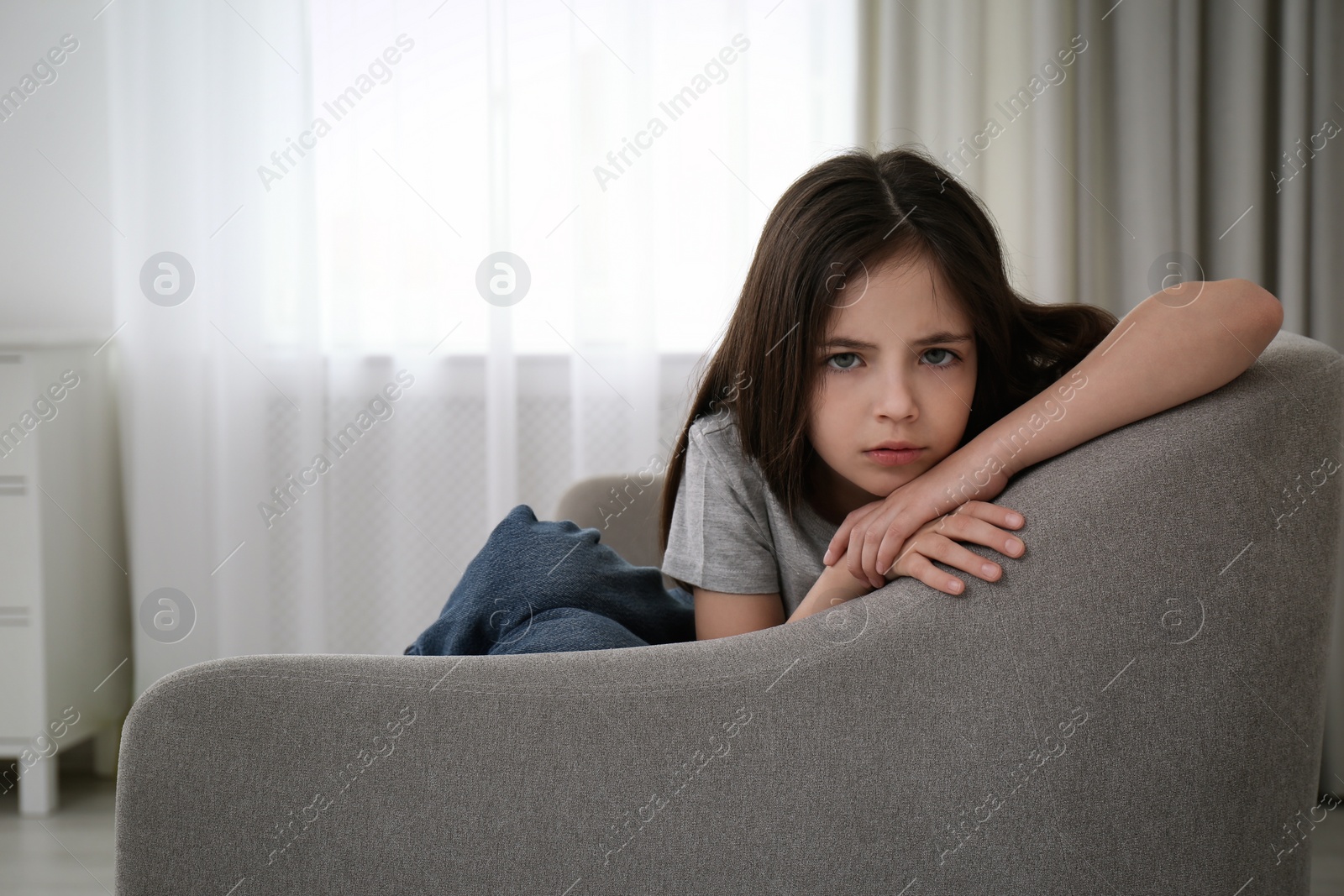 Photo of Sad little girl sitting on sofa indoors, space for text