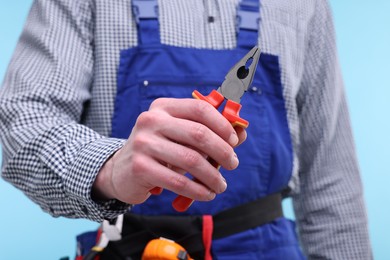 Photo of Young man holding pliers on light blue background, closeup