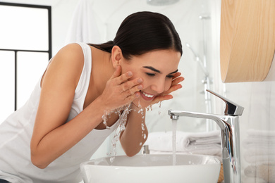 Young woman washing face with cosmetic product in bathroom