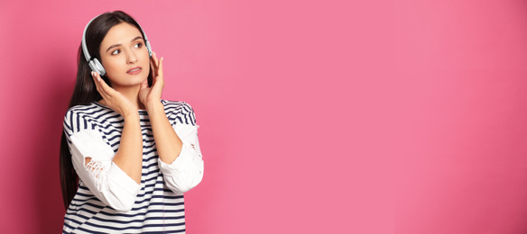 Young woman listening to music with headphones on pink background, space for text. Banner design