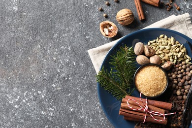 Different aromatic spices and fir branches on grey textured table, flat lay. Space for text