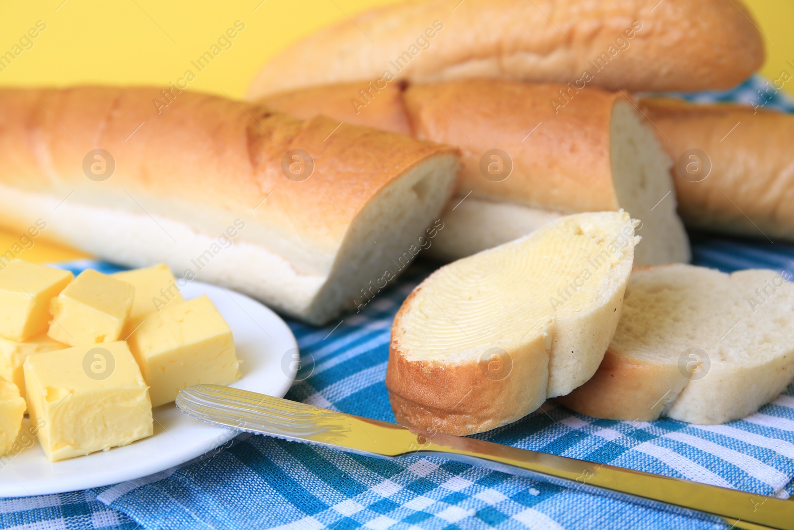 Photo of Whole and cut baguettes with fresh butter on yellow background, closeup