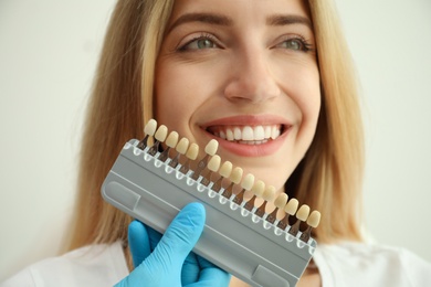 Photo of Doctor matching patient's teeth color with palette on white background, closeup. Cosmetic dentistry