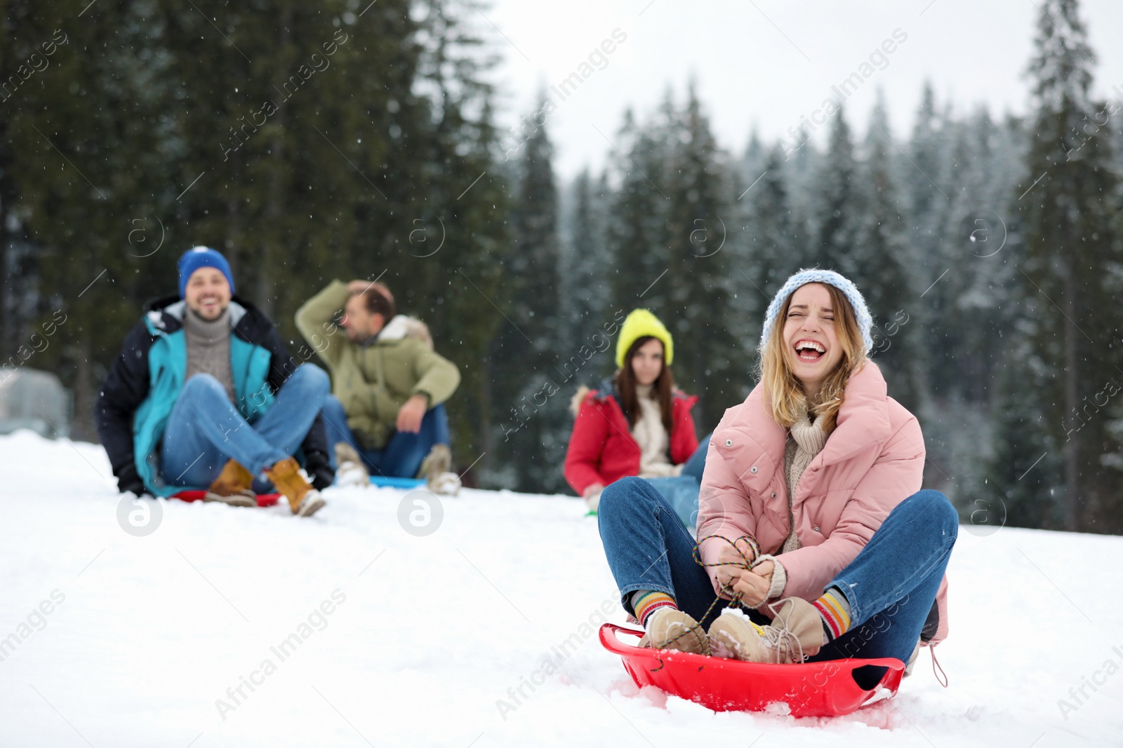 Photo of Happy friends sliding on sleds outdoors. Winter vacation