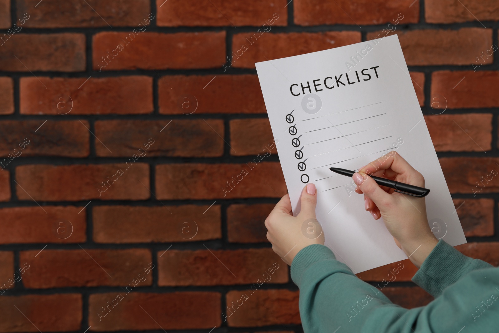 Photo of Woman filling Checklist against brick wall, closeup. Space for text