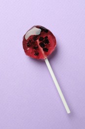 Photo of Sweet colorful lollipop with berries on lilac background, top view