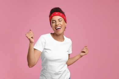 Photo of Happy young woman in stylish headband dancing on pink background