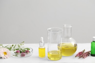 Photo of Cosmetic oil, laboratory dishware and flowers on white table