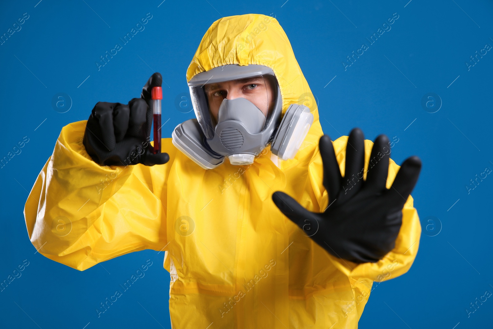 Photo of Man in chemical protective suit holding test tube of blood sample on blue background. Virus research