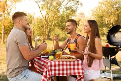 Happy young people having picnic at table in park