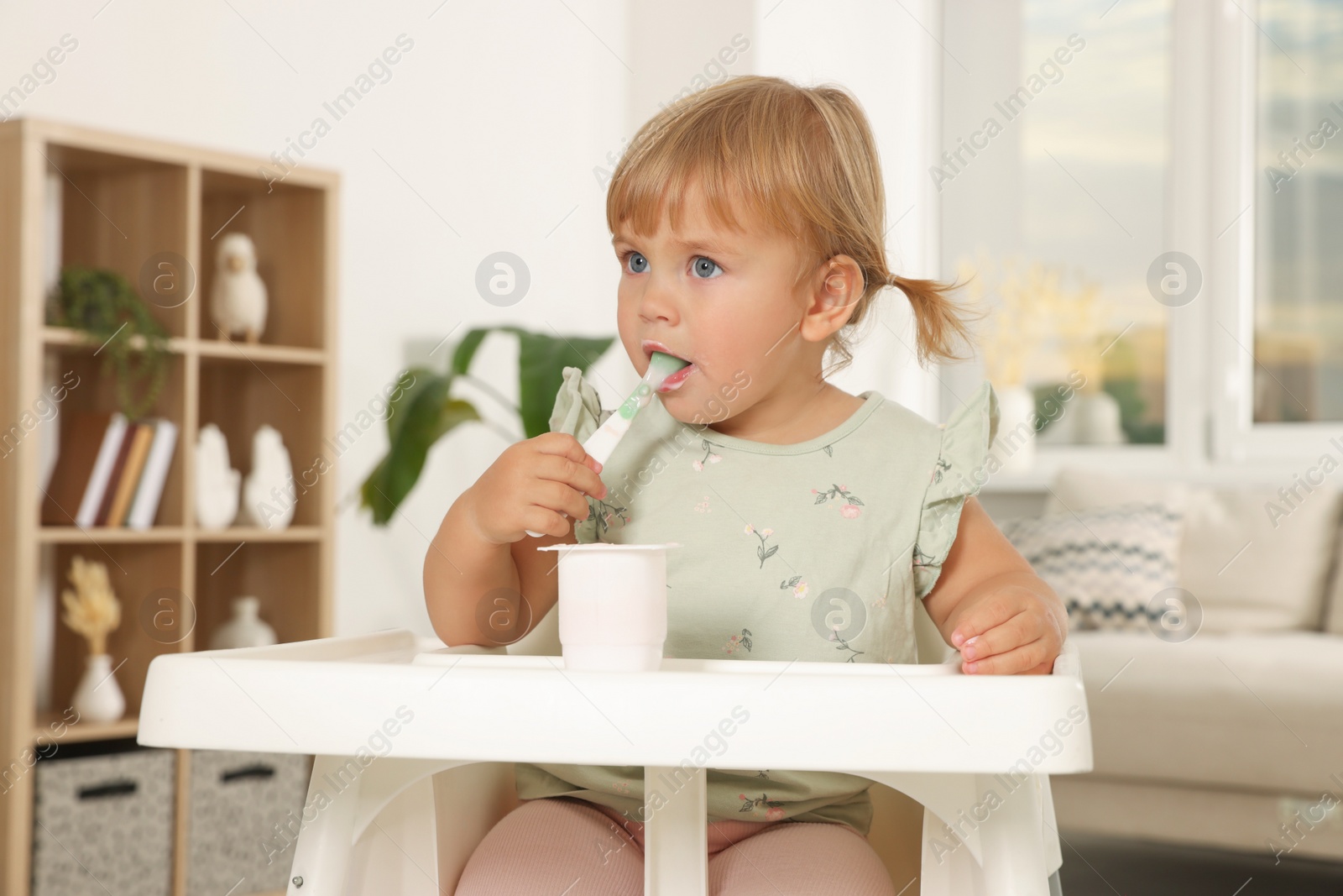 Photo of Cute little child eating tasty yogurt with spoon at home