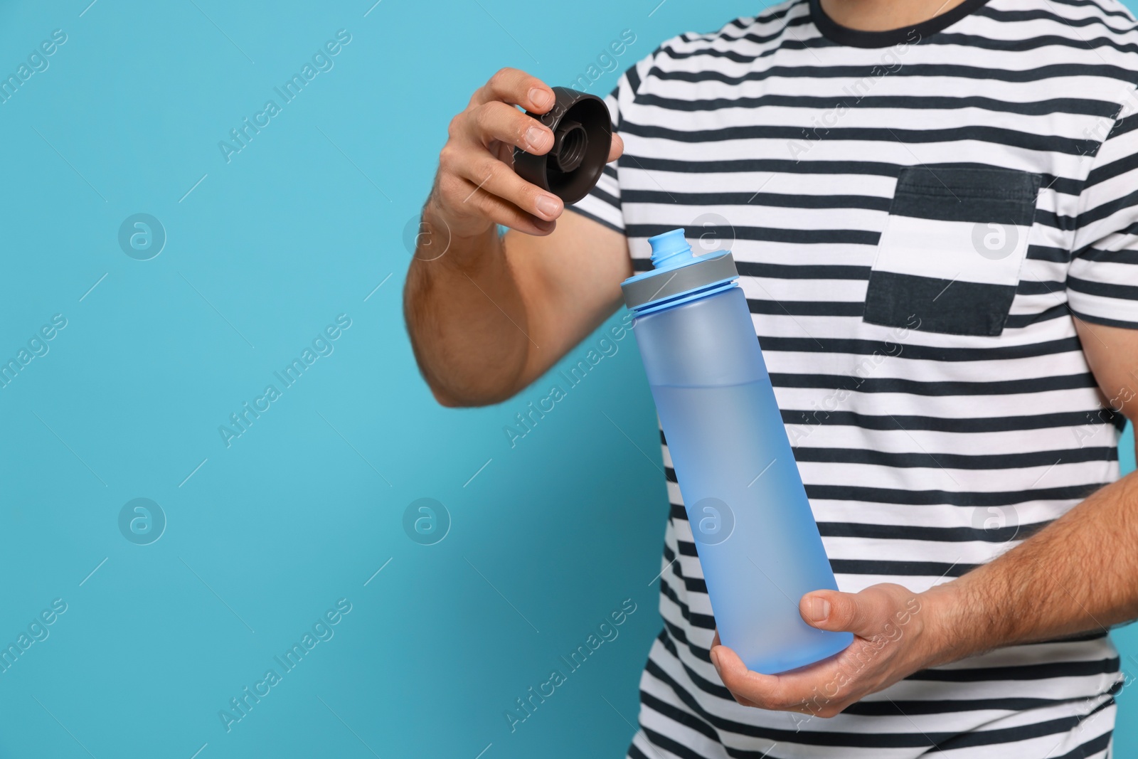 Photo of Man opening transparent plastic bottle with water on light blue background, closeup. Space for text