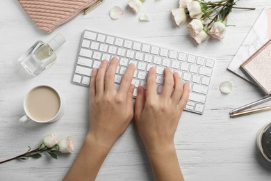 Woman typing on keyboard at table with beautiful roses, top view