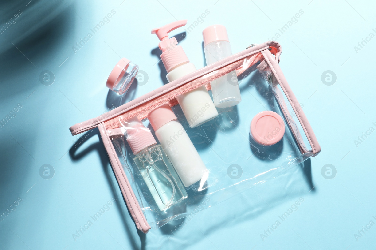 Photo of Cosmetic travel kit with plastic bag on light blue background, top view