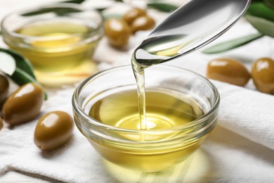 Spoon with cooking oil over bowl and olives on white wooden table, closeup