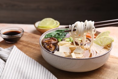 Photo of Eating delicious vegetarian ramen with chopsticks at table, closeup