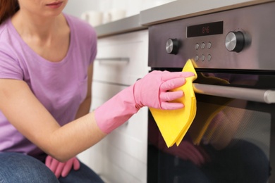 Photo of Woman cleaning oven with rag in kitchen, closeup