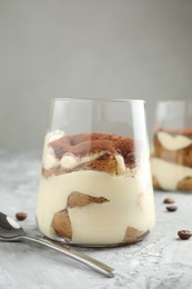 Photo of Delicious tiramisu in glass and spoon on grey textured table, closeup