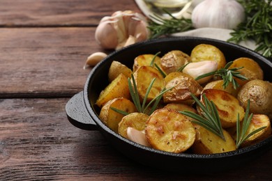 Delicious baked potatoes with rosemary in frying pan on wooden table. Space for text