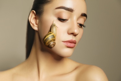 Photo of Beautiful young woman with snail on her face against beige background, closeup