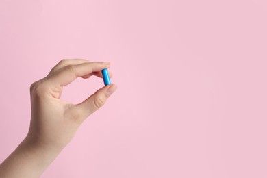 Woman holding pill on pink background, closeup. Space for text