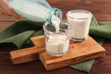 Photo of Pouring milk from bottle into glass at wooden table, closeup