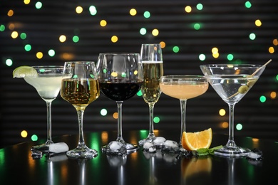 Many different alcoholic drinks on table against dark background with blurred lights