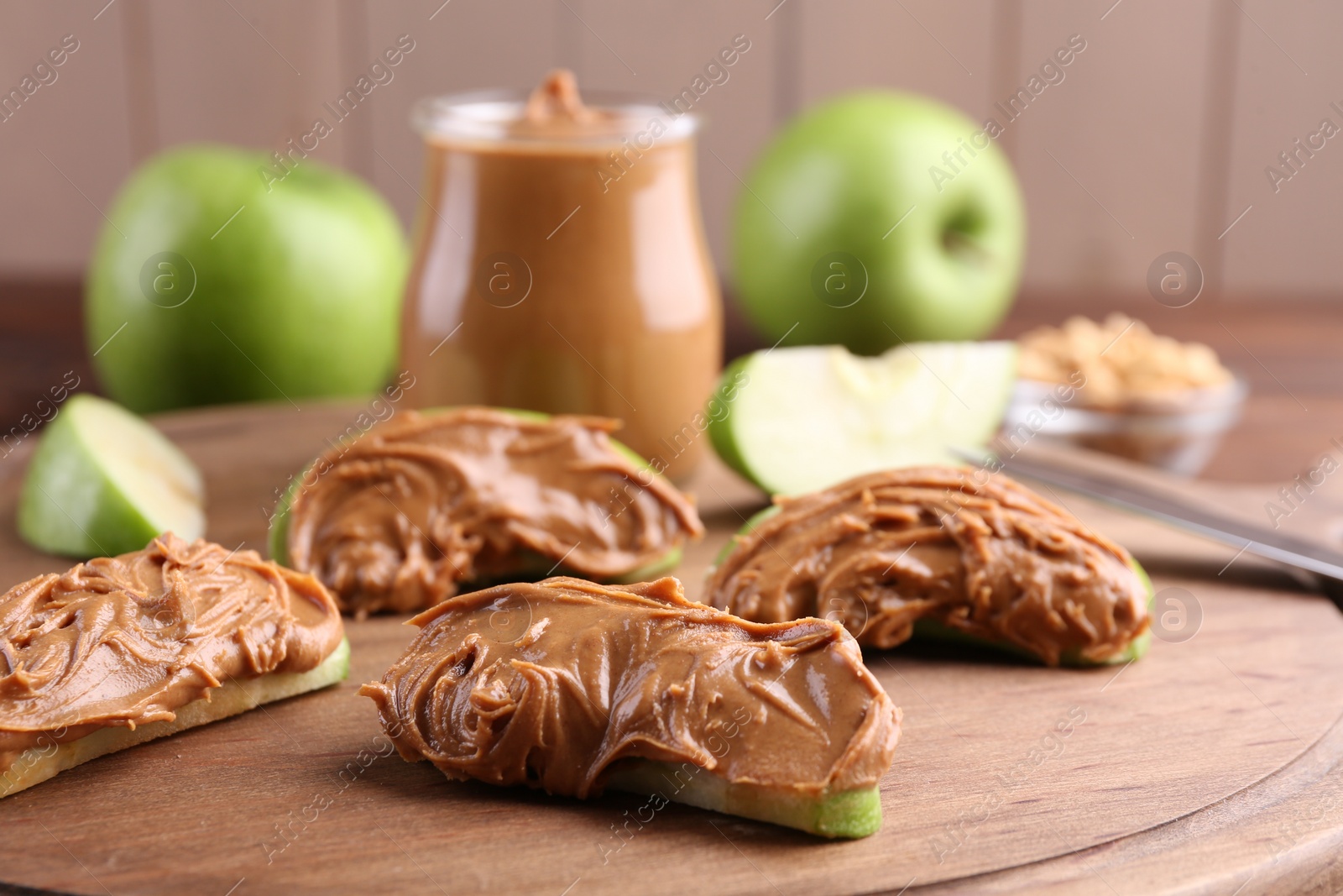 Photo of Slices of fresh green apple with peanut butter on wooden board, closeup