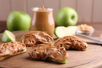 Photo of Slices of fresh green apple with peanut butter on wooden board, closeup