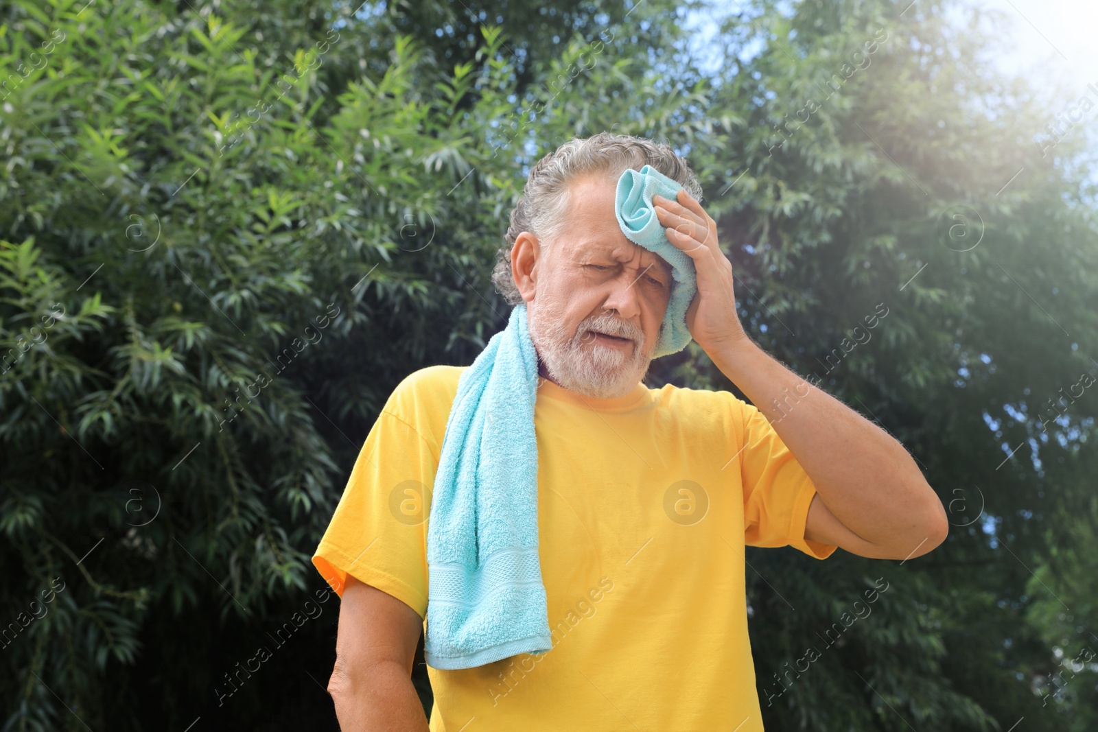 Photo of Senior man with towel suffering from heat stroke outdoors