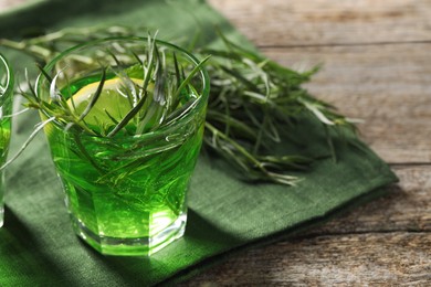 Photo of Glass of refreshing tarragon drink with lemon slice on wooden table. Space for text