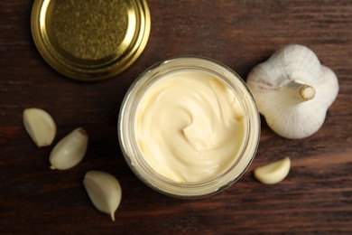 Photo of Jar of delicious mayonnaise and fresh garlic on wooden table, flat lay