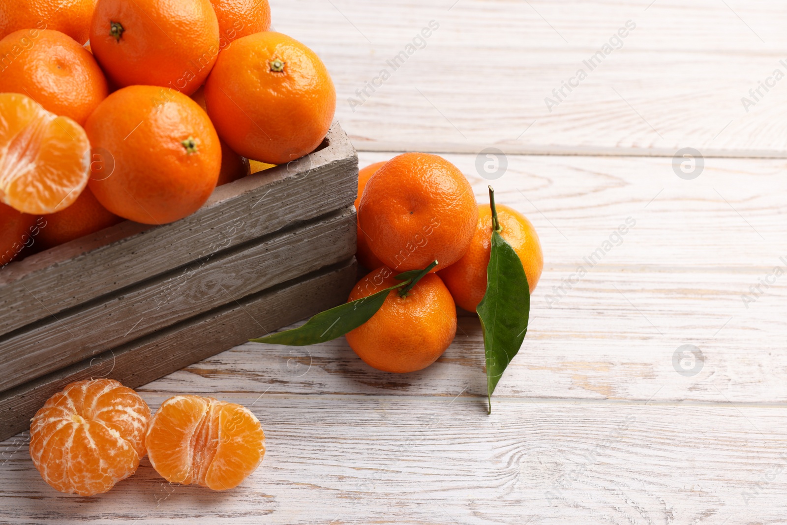 Photo of Delicious tangerines with leaves on light wooden table. Space for text