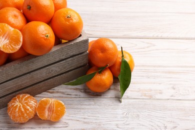 Delicious tangerines with leaves on light wooden table. Space for text