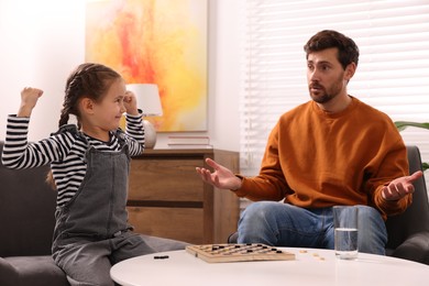 Father playing checkers with his happy daughter at home