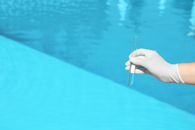Photo of Woman holding glass tube with sample of swimming pool water to check PH level outdoors, closeup. Space for text