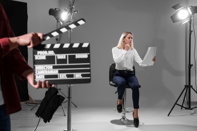 Photo of Casting call. Emotional woman performing while second assistance camera holding clapperboard against grey background in studio