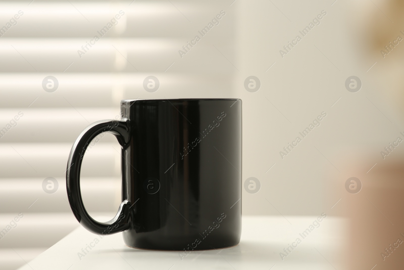 Photo of Black mug on white table indoors. Mockup for design